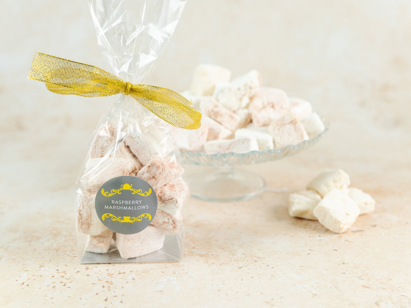 A bag of sweet reason rapberry marshmallows tied with a gold ribbon, with a plate of marshmallows in the background