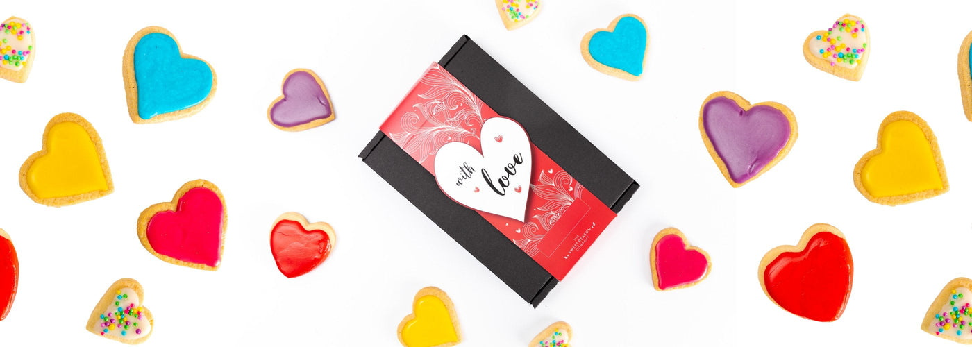 With Love Valentines Gift Box surrounded by brightly coloured iced heart shaped biscuits 