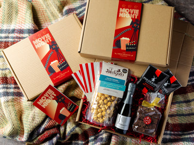 Movie Night Inspired Hamper Containing Alcohol, Popcorn & Brownies. Laid Out On A Traditional Chequered Blanket. 